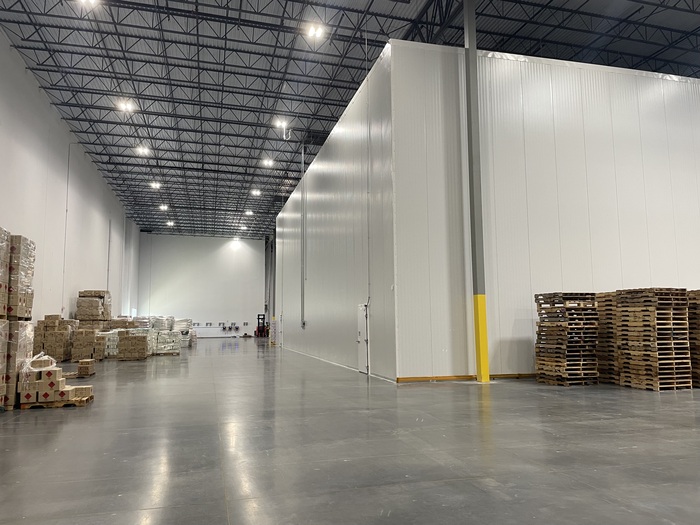 Warehouse interior with insulated storage area, polished concrete floor, palletized products, and high ceiling lighting.