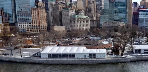 Commercial construction tent structure along the NYC waterfront with downtown Manhattan skyline in the background.