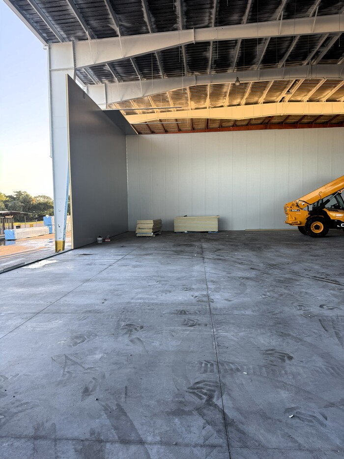 Interior view of a commercial metal building under construction with wall panels, concrete flooring, and equipment.
